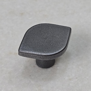 Könnte beinhalten: Ein dunkelgrauer Schrankknauf in Blattform. Der Knauf hat eine abgerundete, strukturierte Oberfläche und einen kurzen, zylindrischen Sockel. Die Hardware ist für den Einsatz an Schubladen oder Schranktüren konzipiert.