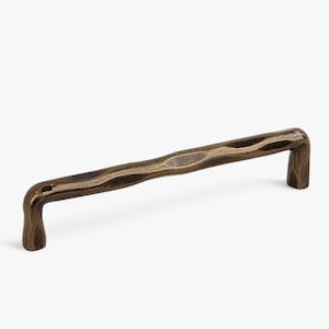 May include: A bronze cabinet pull with a textured, organic design. The handle has a curved shape with a hammered appearance, and is mounted on two short, rectangular posts. The hardware is designed for use on drawers or cabinet doors.