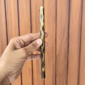 May include: A bronze-colored, textured cabinet pull with a dark brown, wood-like appearance. The handle is held vertically, showcasing its unique, organic design. The hardware is likely for furniture or cabinetry.
