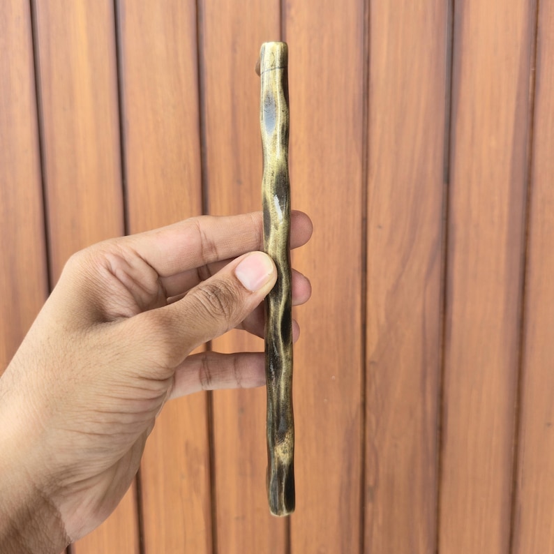 May include: A bronze-colored, textured cabinet pull with a dark brown, wood-like appearance. The handle is held vertically, showcasing its unique, organic design. The hardware is likely for furniture or cabinetry.