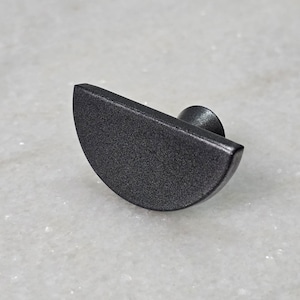 Op de afbeelding: Een donkergrijze, halfronde kastknop met een getextureerd oppervlak. De knop heeft een kleine, ronde basis voor montage. Deze hardware is geschikt voor laden, kasten of ander meubilair.
