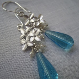 Puede incluir: Pendientes de plata con un racimo de pequeños abalorios de flores y cuentas de vidrio azul en forma de lágrima.