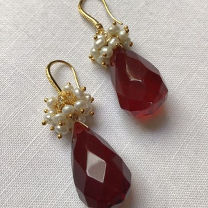 May include: A pair of gold earrings with red teardrop-shaped crystals and clusters of white pearls.