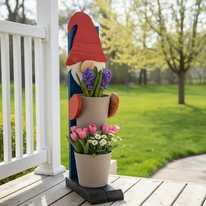 May include: A vertical wooden garden display featuring a red gnome hat, a blue post, and two beige planters. The top planter holds purple hyacinths, while the bottom planter contains pink tulips and white daisies with yellow centers.
