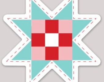 May include: A star-shaped sticker featuring a quilt block design. The star has a light blue background with a white border and red dashed stitching. The center of the star has a red, pink, and white checkered pattern.