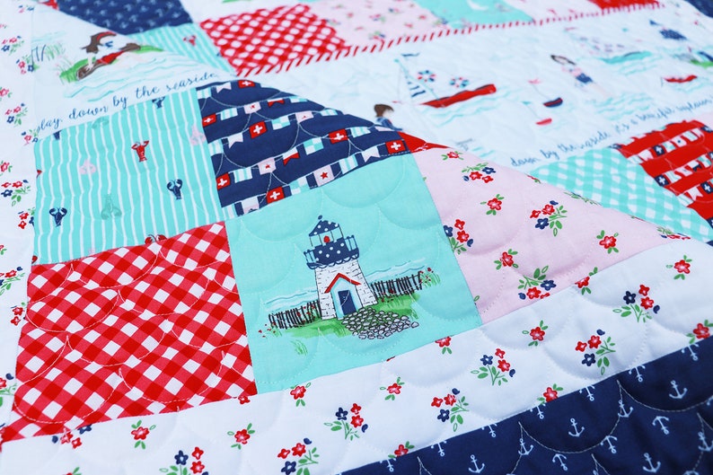 Pode incluir: Uma colcha de retalhos com tema n&aacute;utico. A colcha apresenta um farol, &acirc;ncoras e o texto "stay down by the seaside".