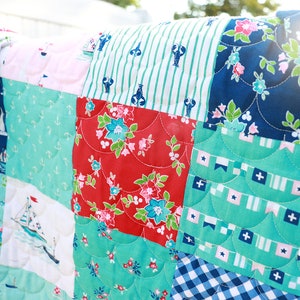 Pode incluir: Uma colcha de retalhos com tema n&aacute;utico. A colcha &eacute; feita de v&aacute;rios tecidos com padr&otilde;es diferentes, incluindo &acirc;ncoras, veleiros, listras e flores. A colcha &eacute; em tons de azul, vermelho, branco e verde.