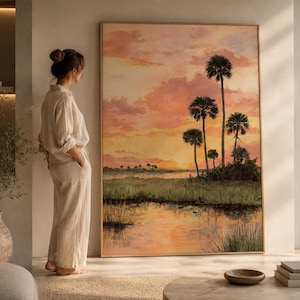 Könnte beinhalten: Ein großes, gerahmtes Landschaftsgemälde zeigt einen Sonnenuntergang über einem Sumpf mit Palmen. Das Kunstwerk weist warme Farben von Orange, Gelb und Rosa im Himmel und im Wasser auf. Das Gemälde wird in einem gut beleuchteten Raum ausgestellt.