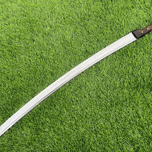 May include: A long, curved sword with a silver blade and a dark wooden handle. The handle is accented with small, gold-colored studs. The sword is set against a backdrop of bright green grass.