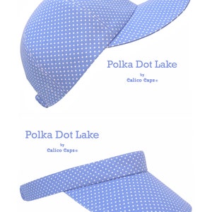 K&ouml;nnte beinhalten: Zwei blaue und wei&szlig;e gepunktete H&uuml;te. Der erste ist eine Baseballkappe und der zweite ist ein Visier. Beide H&uuml;te sagen "Polka Dot Lake by Calico Caps".