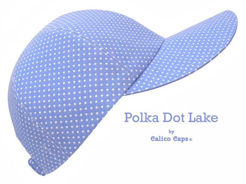 K&ouml;nnte beinhalten: Eine hellblaue Baseballkappe mit wei&szlig;en Punkten. Die Kappe hat einen gebogenen Schirm und ist aus einem weichen, bequemen Stoff gefertigt. Der Text "Polka Dot Lake by Calico Caps&reg;" ist auf der Vorderseite der Kappe aufgedruckt.