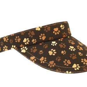 May include: A brown visor with a paw print pattern. The visor is made of fabric and has a curved brim.