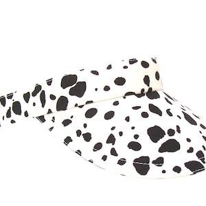 May include: A white visor with a black dalmatian print. The visor has a curved brim and a wide band.