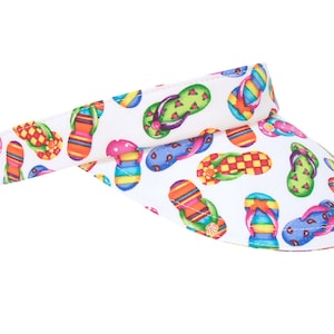 May include: White visor with a colorful flip-flop print. The visor is made of a lightweight fabric and has a curved brim.