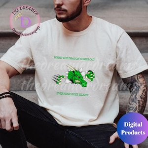 Peut inclure: Un t-shirt blanc avec un dragon vert qui sort du tissu. Le texte "When the dragon comes out, everyone goes silent" est imprimé sur le t-shirt.