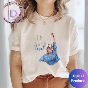 May include: A white t-shirt with a graphic of a woman with a ponytail wearing a blue denim jacket and raising her fist in the air. The text "I'm on a new level" is printed on the shirt.