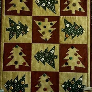 以下が含まれることがあります： クリスマスをテーマにしたパッチワークデザインのキルト。キルトは9つの正方形で構成され、それぞれにクリスマスツリーのアップリケが施されています。木にはボタンが飾られ、金とブルゴーニュの背景に配置されています。