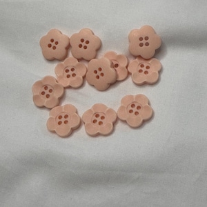 May include: A group of ten peach-coloured flower-shaped buttons with four holes each.