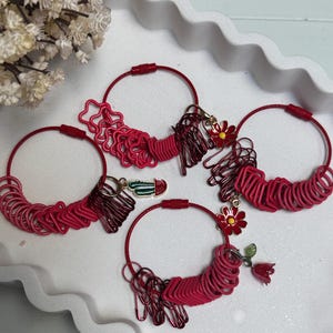 May include: A selection of red ring sizers and keyrings with decorative charms. The ring sizers are arranged in a circular pattern, with charms including flowers and a cactus. The keyrings are red and gold.