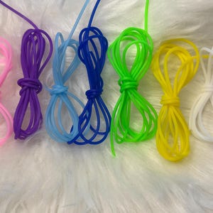 May include: A collection of seven flexible, smooth cords arranged in a row, featuring vibrant colours including pink, purple, light blue, dark blue, neon green, yellow, and white. Each cord is looped into a figure-eight shape with extended ends.