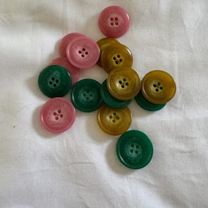 May include: A collection of buttons in pink, green and yellow. The buttons have four holes each and are arranged in a random pattern.