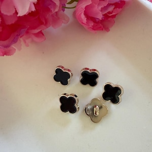 May include: Five clover-shaped buttons featuring a smooth black centre inlay surrounded by a metallic silver-toned border. Each button has a four-leaf design, and one button is flipped over to reveal the metallic silver-toned shank on the back.