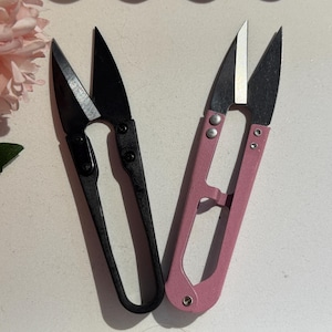 Könnte beinhalten: Zwei Fadenschneider-Paare werden gezeigt. Ein Paar ist schwarz, das andere rosa. Die Klingen sind silberfarben. Die Schneider sind zum Schneiden von Fäden und kleinen Materialien in Näh- und Bastelprojekten bestimmt.