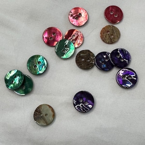 May include: Assortment of colourful shell buttons in various shades of green, purple, brown, and pink. The buttons have two holes and are perfect for sewing projects.