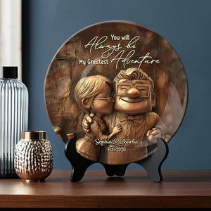 Puede incluir: Un plato de cerámica decorativo con una imagen esculpida en 3D de una pareja, inspirado en la película Up. El plato presenta el texto "You will always be my greatest adventure" y "Sophia & Charlie Est. 2020".