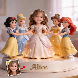 Puede incluir: Una figura decorativa con una niña rodeada de figuras de princesas de Disney. Las princesas son Blancanieves, Cenicienta, Bella y Ariel. La base es blanca con el nombre "Alice" en letras doradas. Una pequeña foto de una niña está en la base.