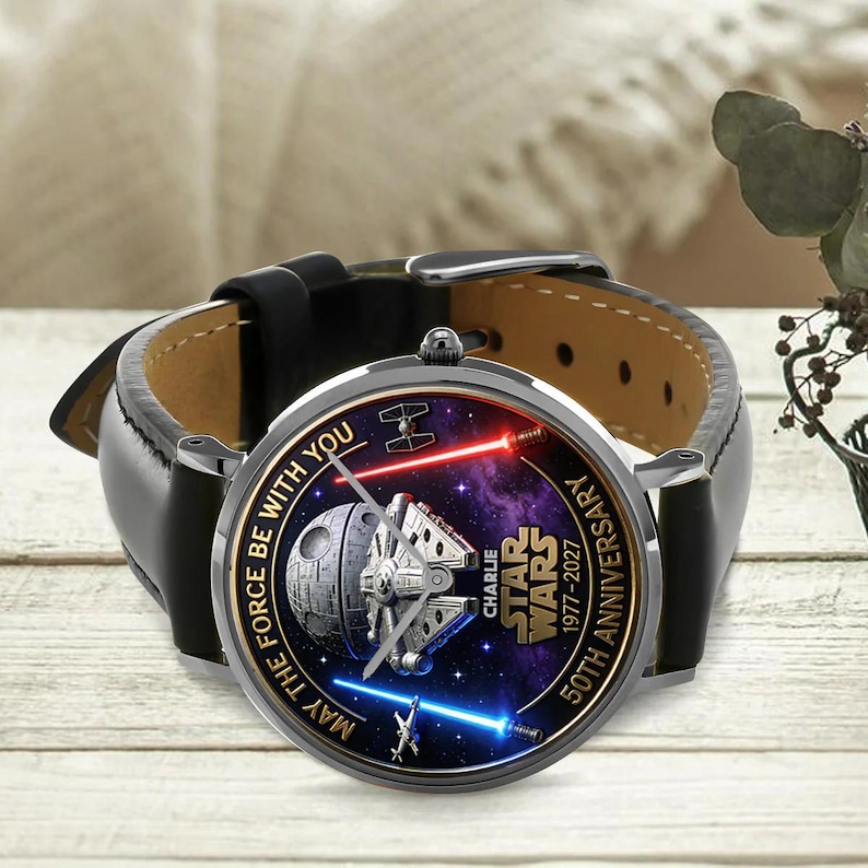 May include: A black leather watch with a Star Wars design. The watch face features the Millennium Falcon, Death Star, and lightsabers against a purple galaxy background. The text reads "MAY THE FORCE BE WITH YOU" and "50TH ANNIVERSARY".