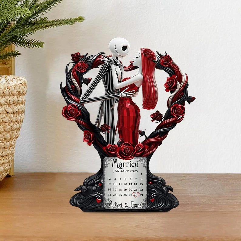 Puede incluir: Una figura decorativa con Jack Skellington y Sally de The Nightmare Before Christmas, abrazados dentro de un marco en forma de coraz&oacute;n con rosas rojas. La base incluye un calendario de enero de 2025, con la palabra "Married" y los nombres "Michael & Emma".
