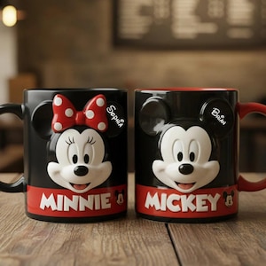 May include: Two black ceramic mugs featuring Mickey and Minnie Mouse. Minnie has a red bow with white polka dots, and the word "MINNIE" in white on a red band. Mickey has the word "MICKEY" in white on a red band.