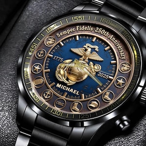 Puede incluir: Reloj de pulsera negro con esfera azul y dorada. La esfera muestra el texto "Semper Fidelis - 250th Anniversary", los años 1775 y 2025, y el nombre "MICHAEL". El reloj tiene una correa de metal negro.