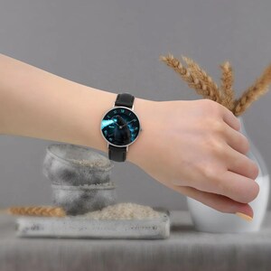 K&ouml;nnte beinhalten: Armbanduhr mit schwarzem Lederarmband und silbernem Geh&auml;use. Das Zifferblatt der Uhr zeigt ein blaues und schwarzes Grafikdesign. Die Uhr wird am Handgelenk getragen.