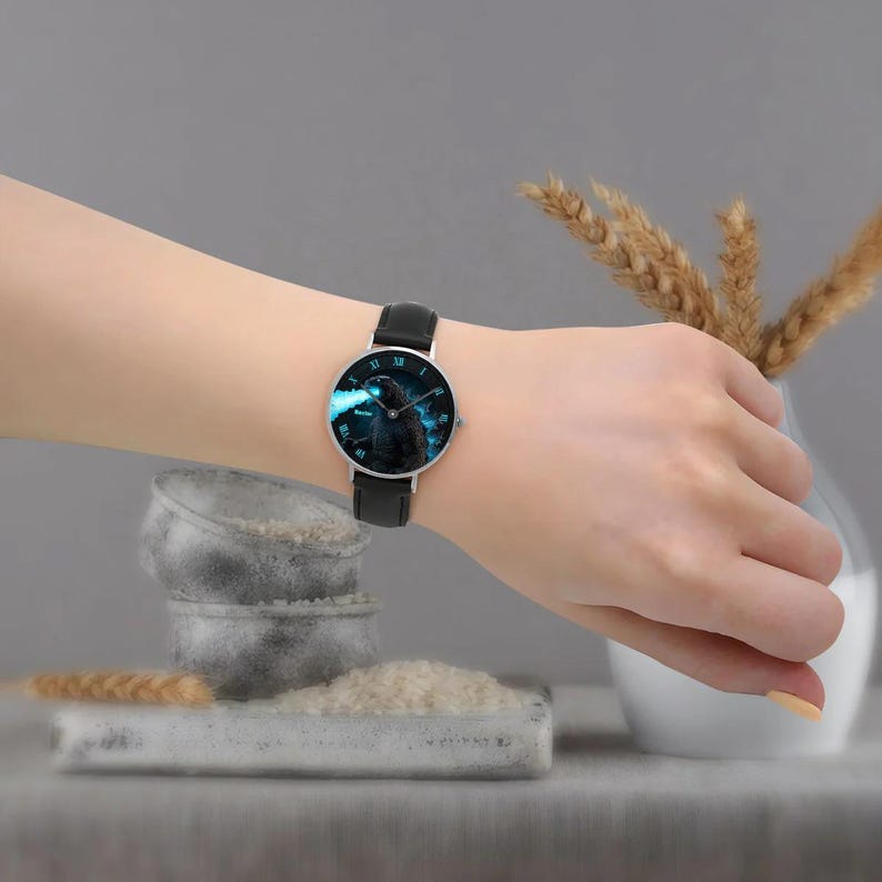 K&ouml;nnte beinhalten: Armbanduhr mit schwarzem Lederarmband und silbernem Geh&auml;use. Das Zifferblatt der Uhr zeigt ein blaues und schwarzes Grafikdesign. Die Uhr wird am Handgelenk getragen.