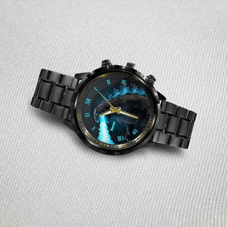 K&ouml;nnte beinhalten: Schwarze Armbanduhr mit Godzilla-Design auf dem Zifferblatt. Die Uhr hat ein schwarzes Metallarmband und ein rundes Zifferblatt mit goldenen Zeigern und r&ouml;mischen Ziffern. Das Zifferblatt hat ein blaues und schwarzes Farbschema.