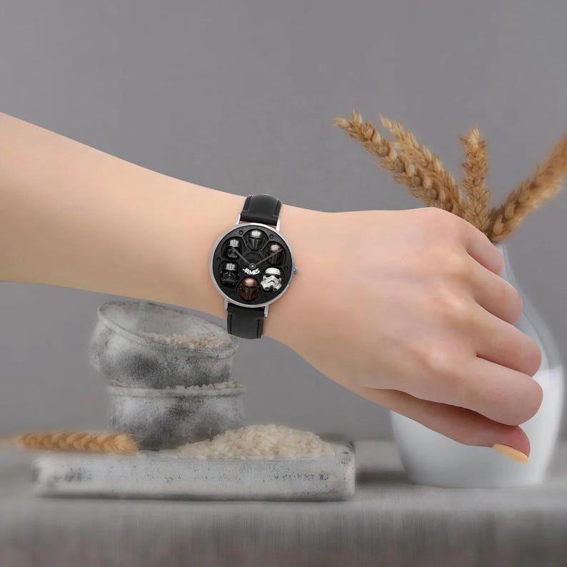 May include: A black leather watch with a silver-colored face featuring Star Wars character designs. The watch has a black leather band and is worn on a wrist.