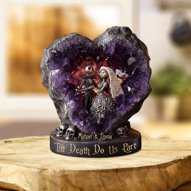 May include: A decorative sculpture featuring Jack Skellington and Sally from The Nightmare Before Christmas, set within a heart-shaped amethyst geode. The base reads "Till Death Do Us Part" with the names "Michael & Emma".