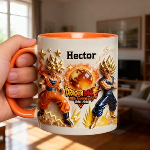 Könnte beinhalten: Eine weiße Keramik-Tasse mit orangefarbenem Griff und Innenraum. Die Tasse zeigt geprägte Bilder von Dragon Ball-Charakteren, den Namen "Hector" und den Text "Dragon Ball 40th Anniversary 1986-2026".