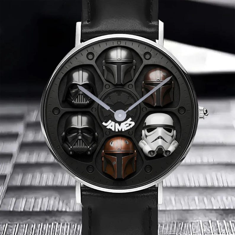 May include: A black wristwatch with a silver bezel and black leather band. The watch face features six character helmets from a popular science fiction franchise, with the word "JAMES" in the center.