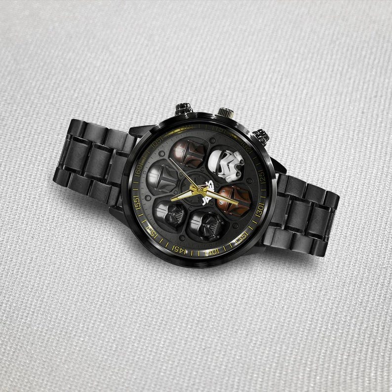 May include: Black wristwatch with a round face featuring various character helmets. The watch has a black metal band and a gold-colored bezel with markings. The watch face includes gold-colored hands and markers.
