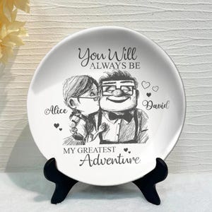 May include: White ceramic plate with a black and white illustration of a couple. The text reads "You Will Always Be My Greatest Adventure" with the names "Alice" and "David" included.