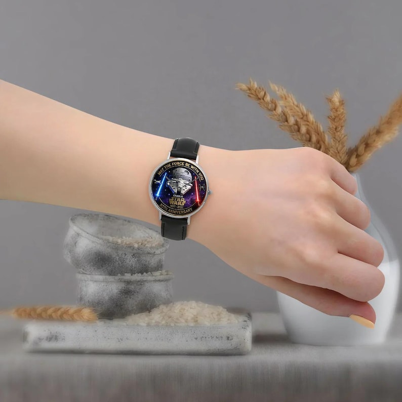 May include: A black leather strap watch with a silver case. The watch face features a Star Wars design with the text "MAY THE FORCE BE WITH YOU" and "STAR WARS 50TH ANNIVERSARY".