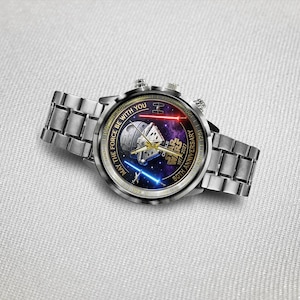 May include: A silver wristwatch with a Star Wars design. The watch face features a space scene with the text "MAY THE FORCE BE WITH YOU" and "50TH ANNIVERSARY". The watch has a silver band and two buttons on the side.