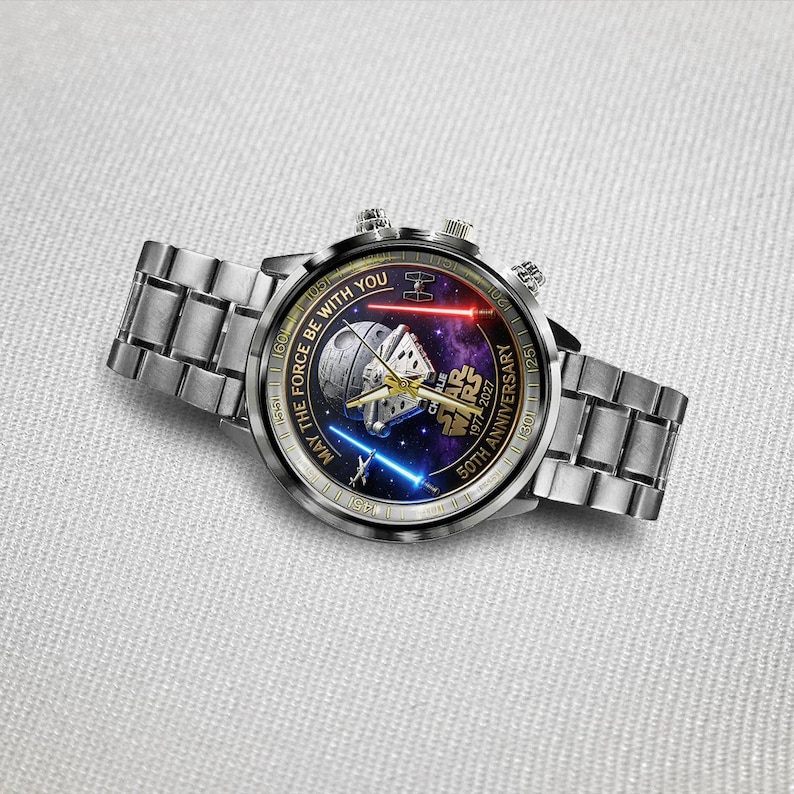 May include: A silver wristwatch with a Star Wars design. The watch face features a space scene with the text "MAY THE FORCE BE WITH YOU" and "50TH ANNIVERSARY". The watch has a silver band and two buttons on the side.
