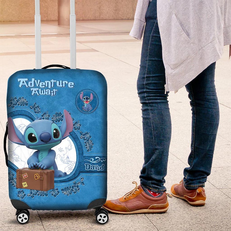 Puede incluir: Maleta rodante azul con Stitch de Lilo & Stitch. La maleta tiene las palabras "Adventure Awaits" y una imagen de dibujos animados de Stitch. Tambi&eacute;n tiene un gr&aacute;fico de maleta marr&oacute;n.