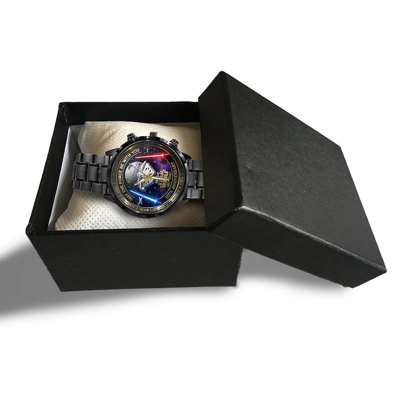 May include: A black wristwatch with a round face featuring a Star Wars design, presented in a black gift box. The watch has a black metal band and a face with a blue and red light saber design. The text "MAY THE FORCE BE WITH YOU" is visible.