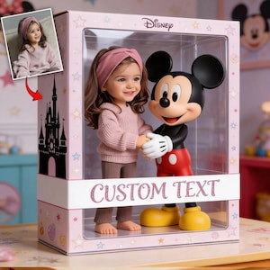 Könnte beinhalten: Eine Disney-Ausstellungsbox mit einer Mickey Mouse-Figur und einer Puppe eines jungen Mädchens. Die Puppe trägt einen rosa Pullover, eine Hose und ein passendes Stirnband. Auf der Box steht der Text "CUSTOM TEXT".