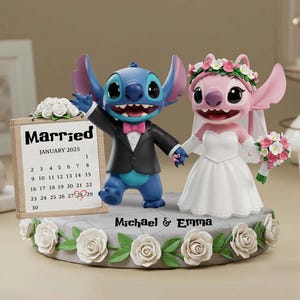 Peut inclure: Une figurine de gâteau de mariage représentant les personnages Stitch et Angel. Stitch porte un smoking et Angel une robe de mariée. Un calendrier indique "Mariés janvier 2025" avec la date encerclée. La base est décorée de roses et des noms "Michael & Emma".